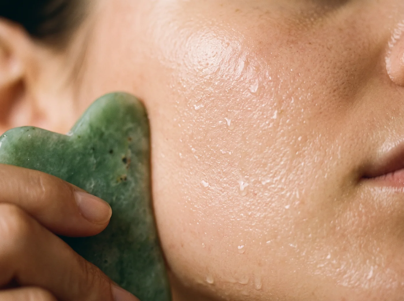 Jade gua sha stone gliding over glowing, freshly hydrated skin during a facial